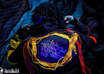Cypher De La Cruz faces away from the camera. He holds his popped collar to display the words Punk You Up on the back of his jacket.